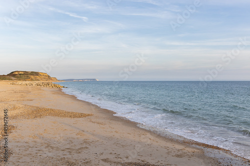 A scenic beautiful view of a sandy beach with blue sea, rocky groyne, majestic hills and golden hours colors under a majestic blue sky and some white clouds