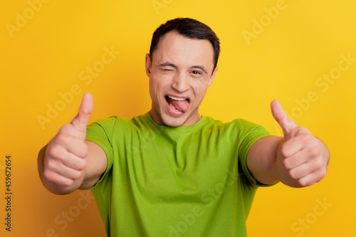 Portrait of funky guy raise two thumbs up open mouth protrude tongue on yellow background © Tetiana
