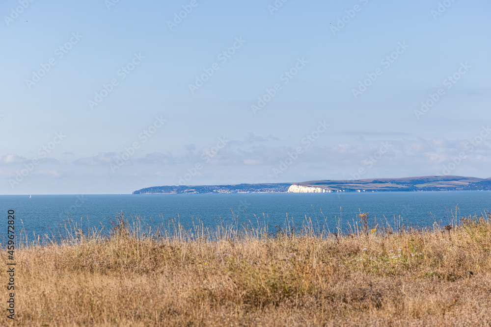 A scenic majestic view of  Bournemouth bay from a grassy cliff under a beautiful blue sky and some white clouds