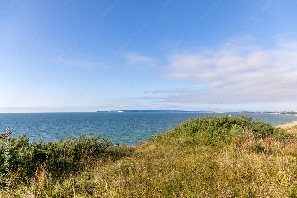 A scenic majestic view of  Bournemouth bay from a grassy cliff under a beautiful blue sky and some white clouds