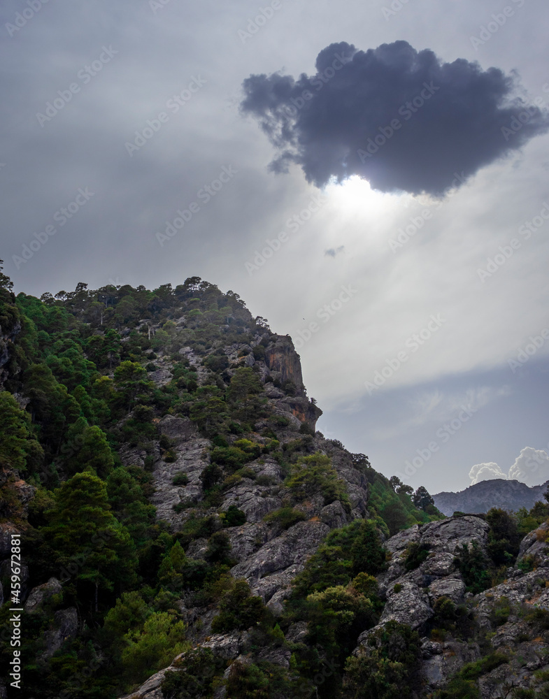 Photograph of a beautiful and majestic landscape in which a large cloud lets some rays of sunlight pass towards the top of that great mountain.
