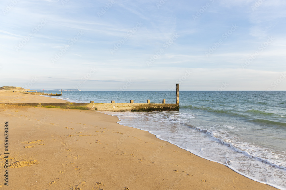 A scenics view of a beautiful sandy beach with a wooden groyne (breakwater) under a blue sky with some white clouds