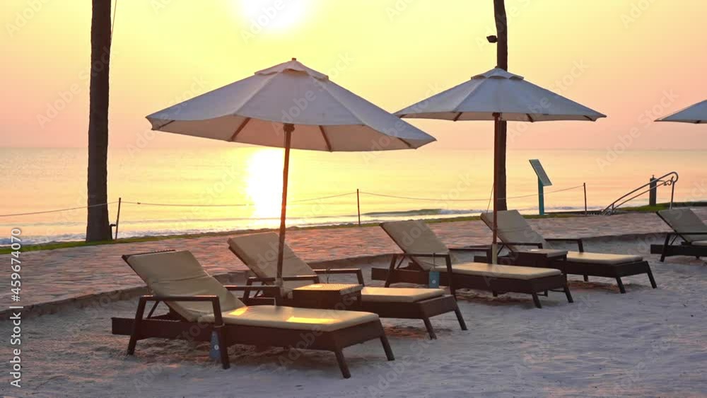 Seafront lounge on the beach with a line of sunbeds under Parasols at golden color sunset over the sea Seafront lounge on the beach with a line of sunbeds under Parasols at golden color sunset over the sea