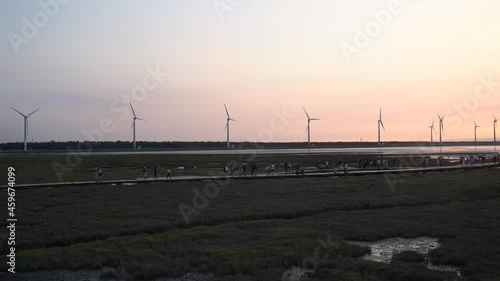 Tourists walking on the platform visiting well preserved remarkable gaomei wetland preservation area in Taichung, Taiwan, with a row of wind turbines in the background against diffused sunset color. photo