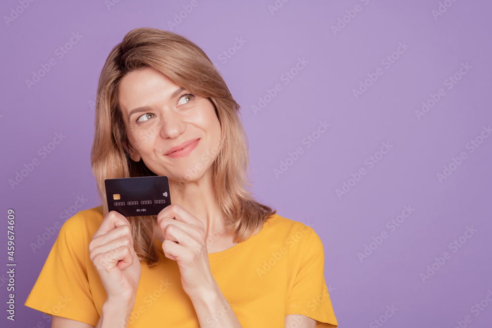Photo of young attractive woman happy positive smile hold credit card dream look empty space isolated on violet color background Photo of young attractive woman happy positive smile hold credit card dream look empty space isolated on violet color background