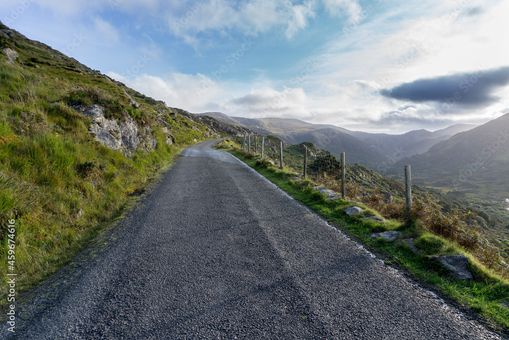 narrow road with asphalt and green grass through hills and valley on the wild Atlantic way in ireland with no cars on it