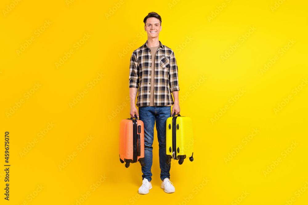 Photo of cheerful positive guy carry two suitcase toothy smile wear plaid shirt isolated yellow color background Photo of cheerful positive guy carry two suitcase toothy smile wear plaid shirt isolated yellow color background