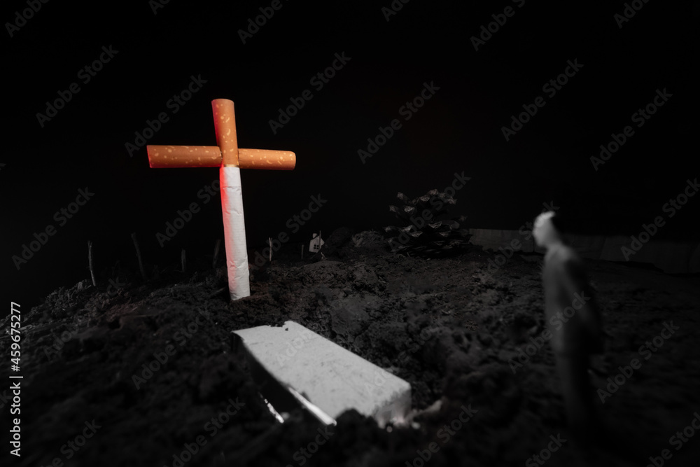 A man looks at the grave with a cross made of cigarettes.