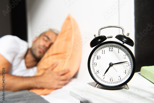 Hispanic man sleeping in the bed and an alarm clock