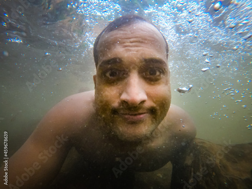 man swimming in natural waterfall underwater shot from low angle