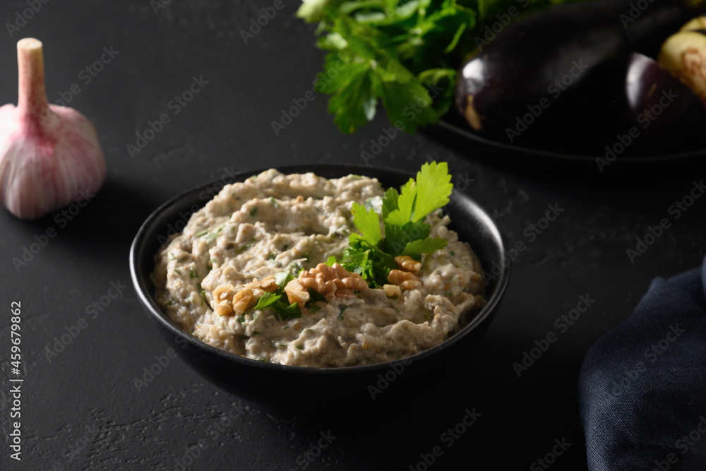 Baba ganoush Asian cuisine appetizer made from baked eggplant with parsley, garlic and olive oil on black table. Close up. Middle Eastern cuisine, vegan hummus. Baba ganoush Asian cuisine appetizer made from baked eggplant with parsley, garlic and olive oil on black table. Close up. Middle Eastern cuisine, vegan hummus.