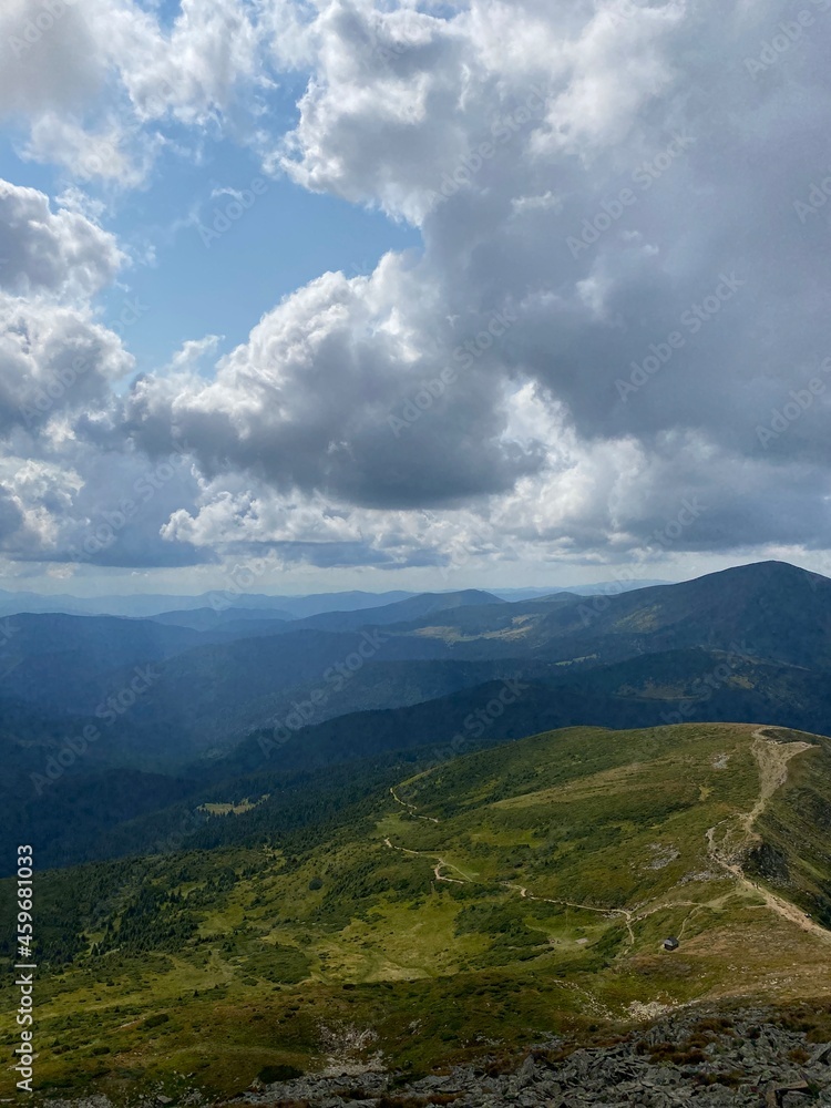 Mountain summer landscape. Trail among the forest against the background of mountain peaks and  sky. View from Makovytsia mountain, Yaremche area. Carpathians. Ukraine.
