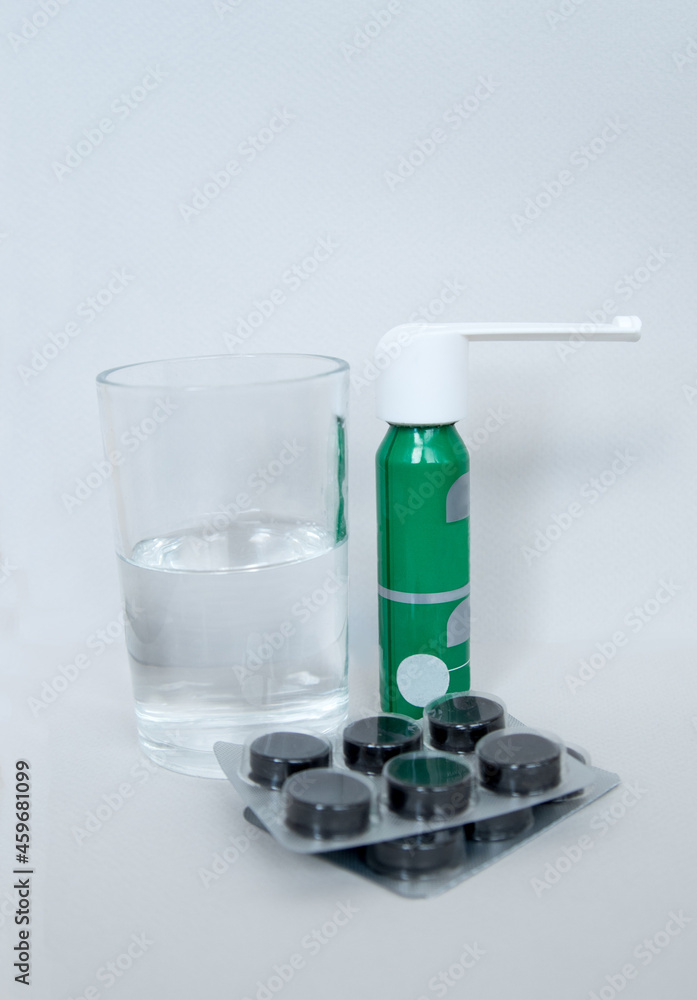 Medicines, tablets and spray with a glass of water on a light background