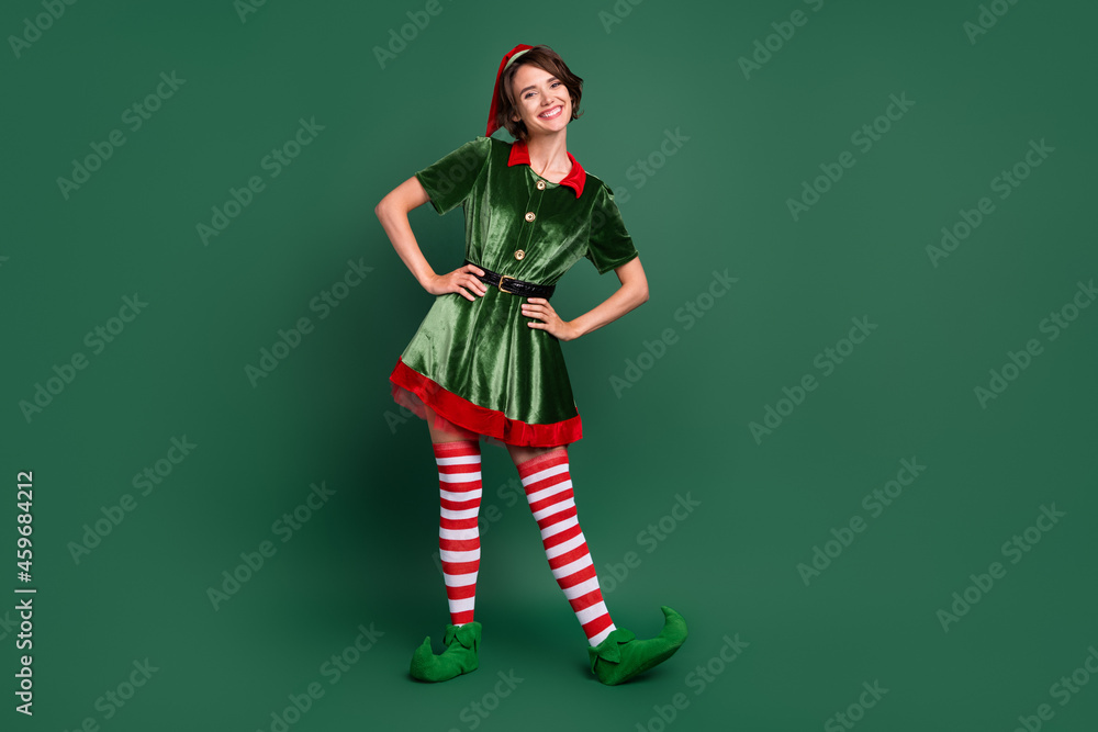 Photo of funny positive cheerful helper lady hands hips wear elf costume hat stockings isolated green color background - obrazy, fototapety, plakaty 