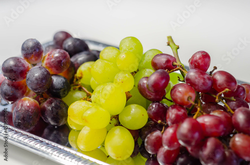 Three types of green, red and black grapes on a silver tray