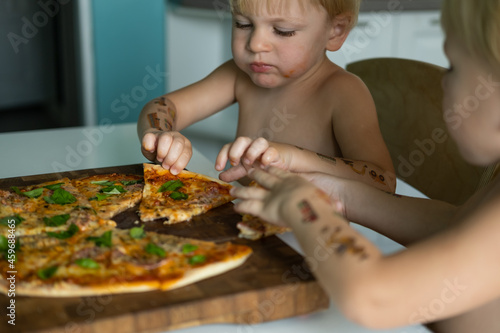 two cute kids twins brothers boy eating home made pizza at kitchen at home