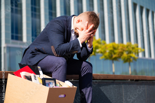 Depleated former employee sitting with his belongings stuffed in a box next to him. photo