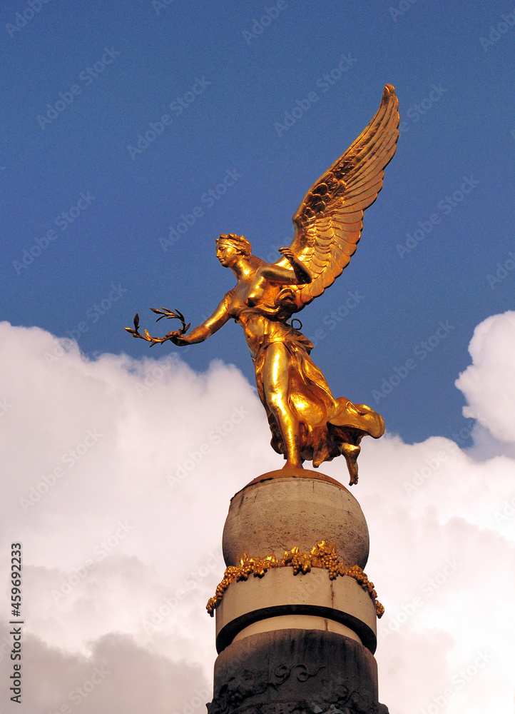 Fototapeta premium Golden Sculpture Of A Young Woman With Wings In Reims In France On A Beautiful Spring Day With Some Clouds In The Blue Sky