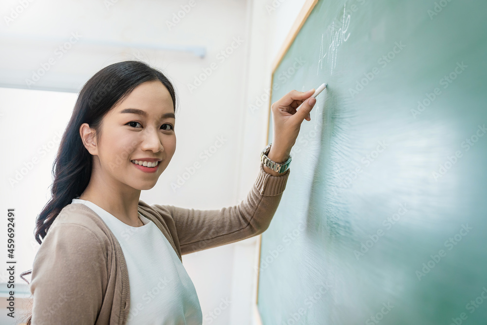 Closeup portrait of young happy asian teacher write on chalk board. Woman writing on blackboard wall. Idea creative education teaching math and spelling letter, knowledge, back to school concept