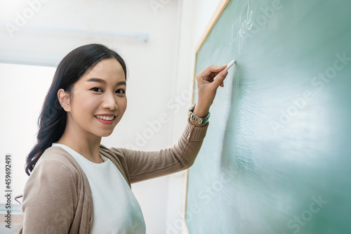 Closeup portrait of young happy asian teacher write on chalk board. Woman writing on blackboard wall. Idea creative education teaching math and spelling letter, knowledge, back to school concept