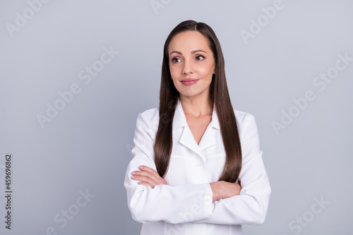Photo of positive dreamy lady doctor wear white formal coat smiling arms folded isolated grey color background