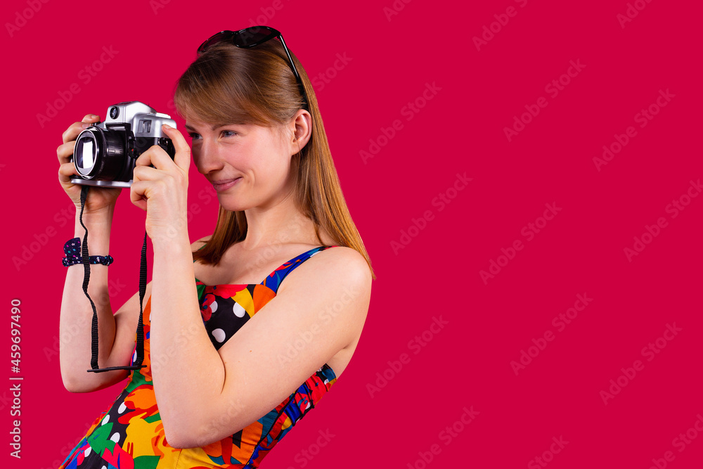 Attractive young blonde female tourist with sunglasses on the head is smiling and making photo on retro camera. Attractive young blonde female tourist with sunglasses on the head is smiling and making photo on retro camera.