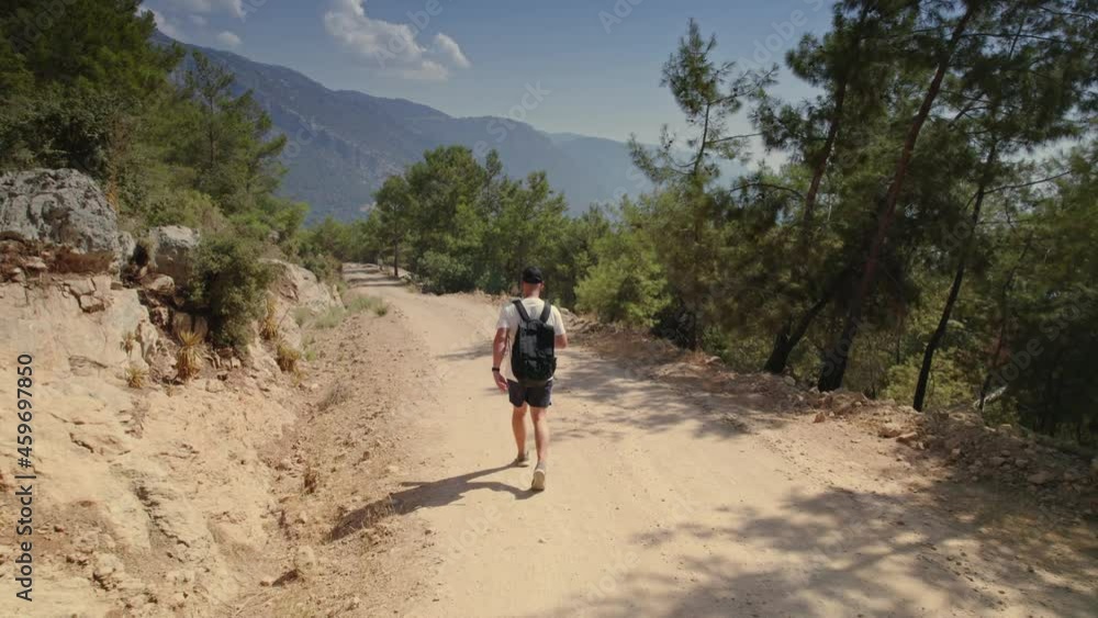 A man traveler with a backpack walks through the highlands, mountain road in the forest, hiking mountain road in the forest, man tracking, aerial footage panorama A man traveler with a backpack walks through the highlands, mountain road in the forest, hiking mountain road in the forest, man tracking, aerial footage panorama