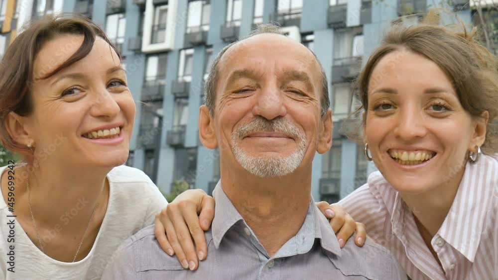 Family portrait of senior father and two adult daughters kissing him outdoors on modern building of new residential complex, fathers day celebration concept Family portrait of senior father and two adult daughters kissing him outdoors on modern building of new residential complex, fathers day celebration concept