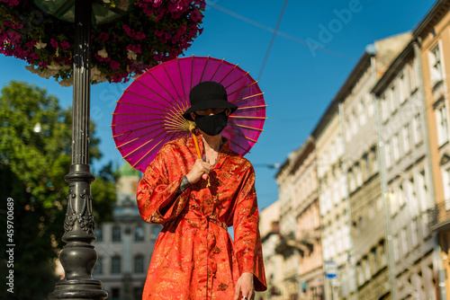 Positive man with dressed in street style clothes red kimono with chains around neck  black panama and black medical mask . Youth and lifestyle concept.