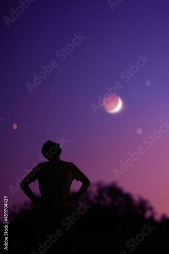 Silhouette of a man and countryside under the starry skies with young Moon.