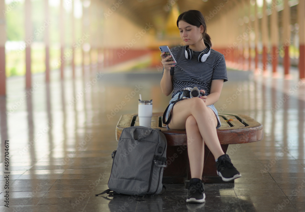 Female traveler looking at smartphone while waiting for a train on platform.