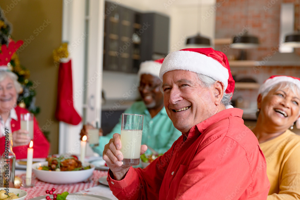 Happy caucasian senior man holding glass and celebrating christmas with diverse group of friends