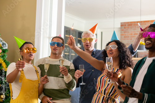 Group of happy diverse female and male friends with whistles and colorful hats celebrating new year