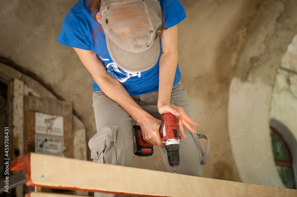 Skilled young female worker is using power screwdriver drilling during construction wooden bench gender equality, feminism, do it yourself concepts. Skilled young female worker is using power screwdriver drilling during construction wooden bench gender equality, feminism, do it yourself concepts.