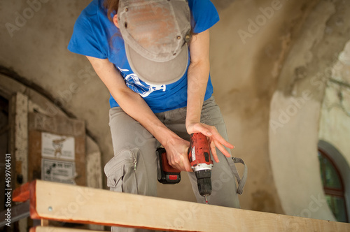 Skilled young female worker is using power screwdriver drilling during construction wooden bench gender equality, feminism, do it yourself concepts.