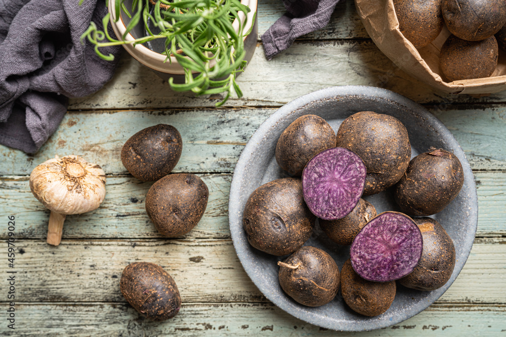 Close up of farm fresh purple potatoes in a bowl on white wooden background, top view Close up of farm fresh purple potatoes in a bowl on white wooden background, top view