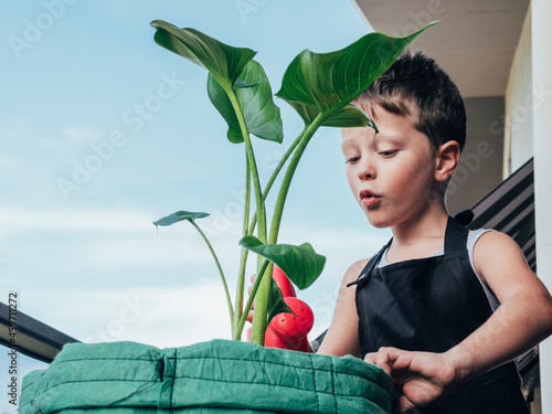 Content boy with watering can and blooming plant on balcony