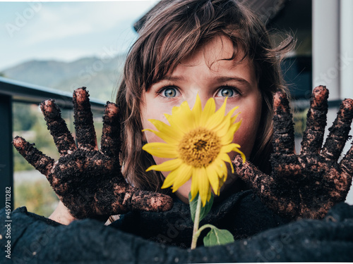 Dirty girl having fun against blooming Helianthus growing in soil