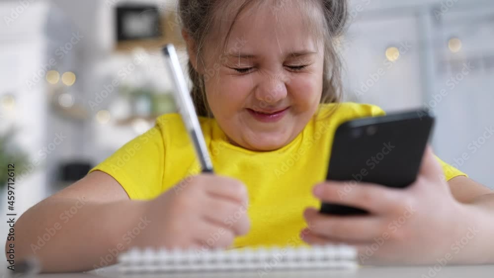 distance learning. online a education. school kid writes in a notebook looks at a smartphone lessons remotely school. kid daughter writes in home a notebook doing homework distance learning distance learning. online a education. school kid writes in a notebook looks at a smartphone lessons remotely school. kid daughter writes in home a notebook doing homework distance learning