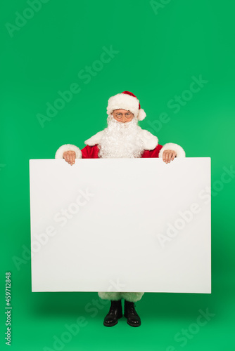 Santa claus holding placard with copy space and looking at camera on green background