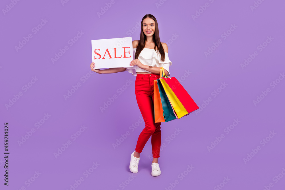 Photo of cheerful lady hold client bargains show sale poster wear white blouse pants isolated violet color background Photo of cheerful lady hold client bargains show sale poster wear white blouse pants isolated violet color background