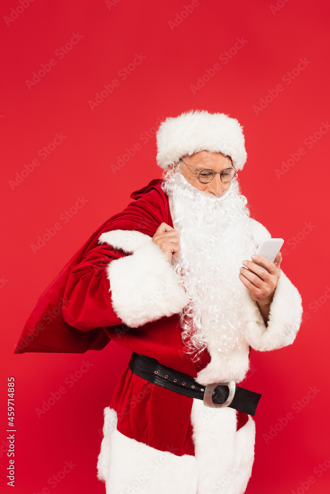 Santa claus with sack using mobile phone isolated on red Santa claus with sack using mobile phone isolated on red