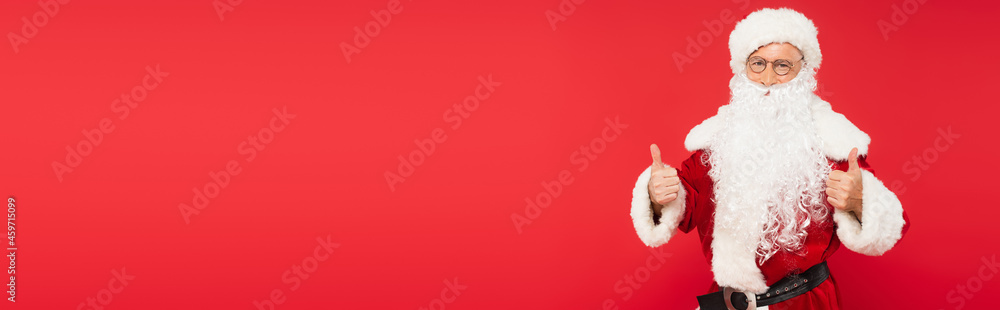 Santa claus in eyeglasses showing thumbs up isolated on red, banner
