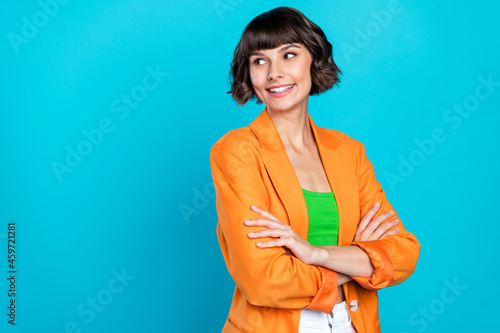 Photo of funny millennial brunette lady crossed arms look empty space wear orange blazer top isolated on teal color background