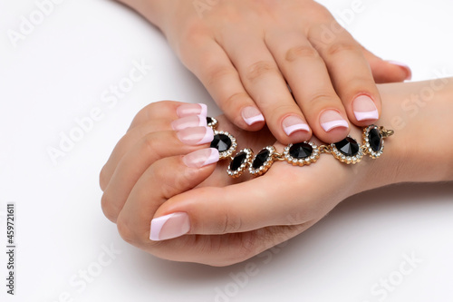 Lilac French manicure on short square nails on a white background close-up. Gel nails. Gold earring with black stones in her hands.