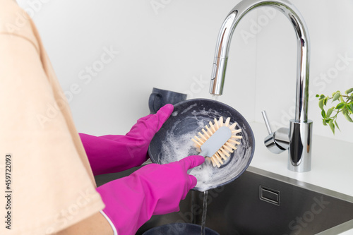 Young woman washes dishes with brush with natural bristles in kitchen.