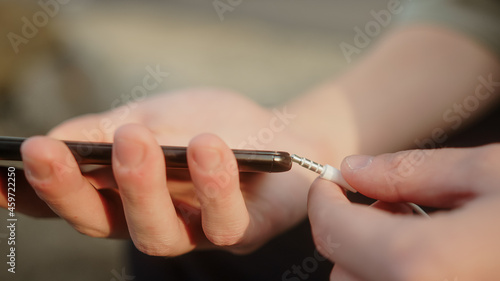 Young man plugging aux input cable into his smartphone, listening to music or making a call close-up