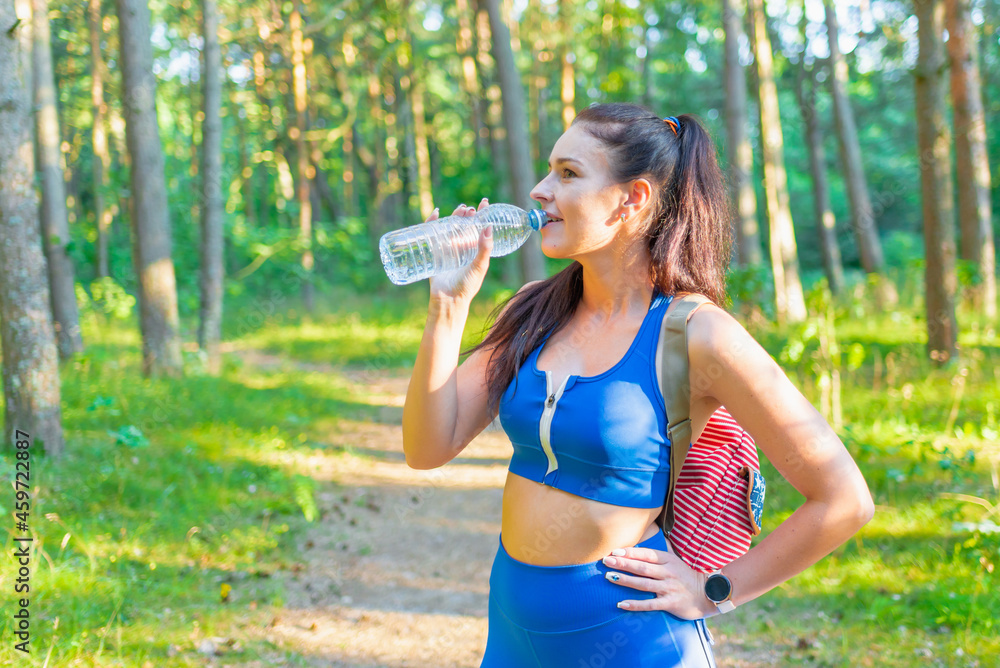 attractive happy young woman hiker with backpack drinking bottled water walking on summer forest trail summer landscape attractive happy young woman hiker with backpack drinking bottled water walking on summer forest trail summer landscape
