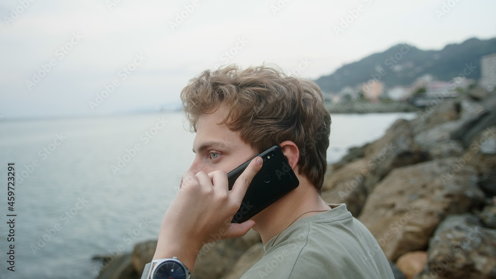 Handsome blond boy making phone call with smartphone by the sea