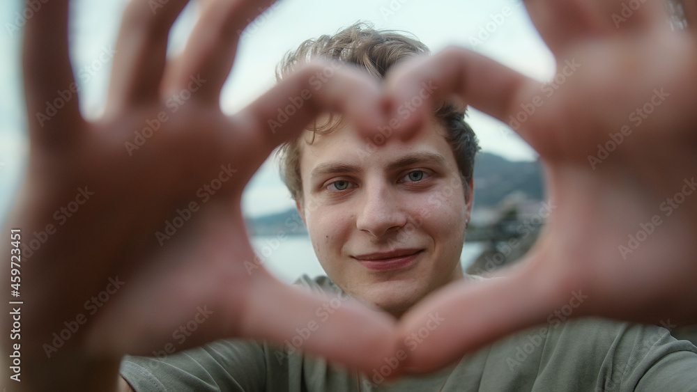 Young blond boy towards camera making heart symbol with hand and smiling looking at camera Young blond boy towards camera making heart symbol with hand and smiling looking at camera